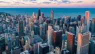 A stunning high-angle aerial view of the downtown Chicago skyline at sunset, with iconic skyscrapers like the John Hancock Center set against the vast expanse of Lake Michigan.
