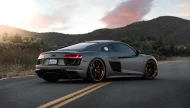 A stunning matte gray Audi R8 supercar with custom black and bronze wheels parked on a winding mountain road during a beautiful sunset.
