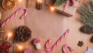 A cozy Christmas flat lay on a wooden background, featuring a blank piece of paper in the center framed by candy canes, dried oranges, pine cones, cinnamon sticks, a rustic gift, and warm fairy lights.