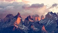 The dramatic granite peaks of Torres del Paine National Park in Patagonia, glowing with fiery orange and red alpenglow during a stunning sunrise.